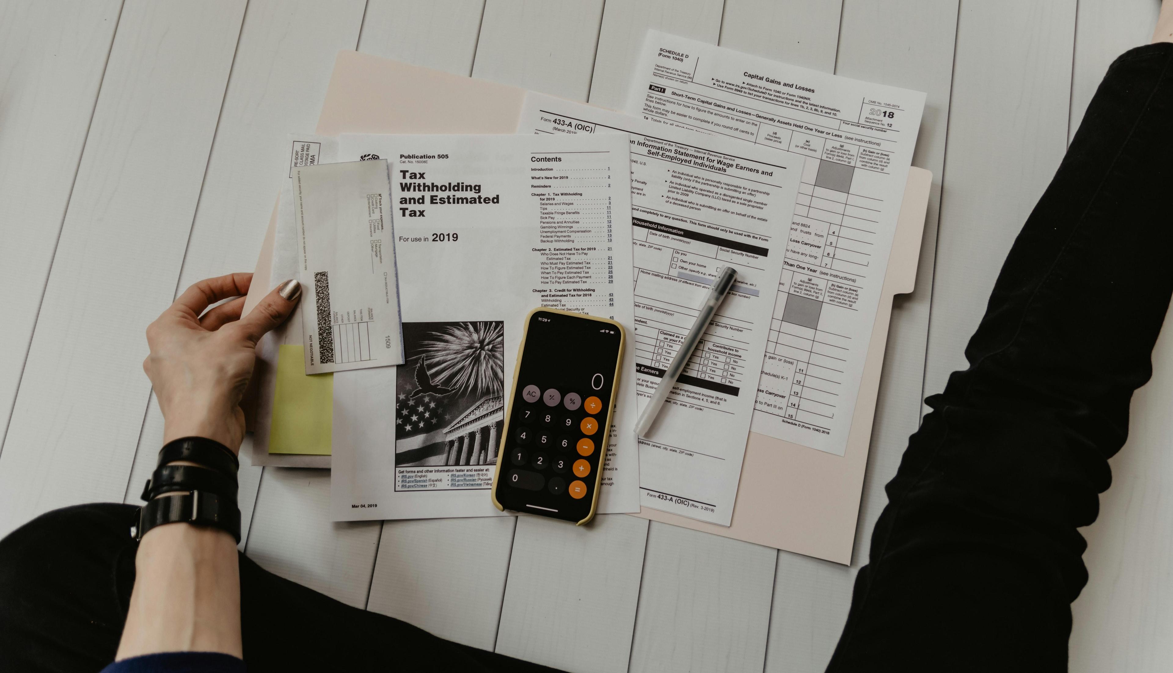 A phone calculator, a pen, and tax documents laid out on the floor.