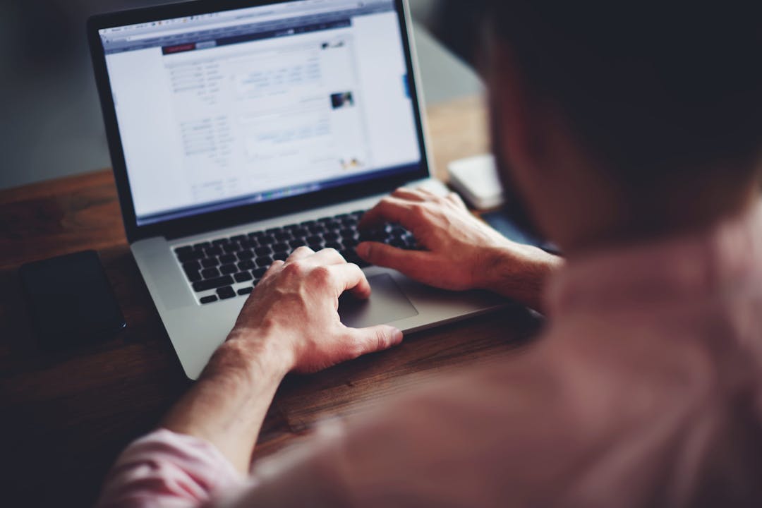 Cropped image of a young man working on his laptop in a coffee shop, rear view of business man hands busy using laptop at office desk, young male student texting on computer sitting at wooden table